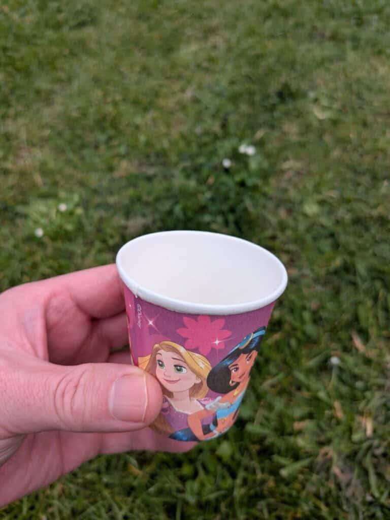 A small paper cup with green grass in the background. Some wonder are paper cups lined with plastic.